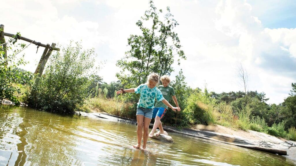 Twee kinderen lopen over stenen in de speelvijver van het Kindvriendelijke familiepark De Lemeler Esch in Lemel in Overijssel