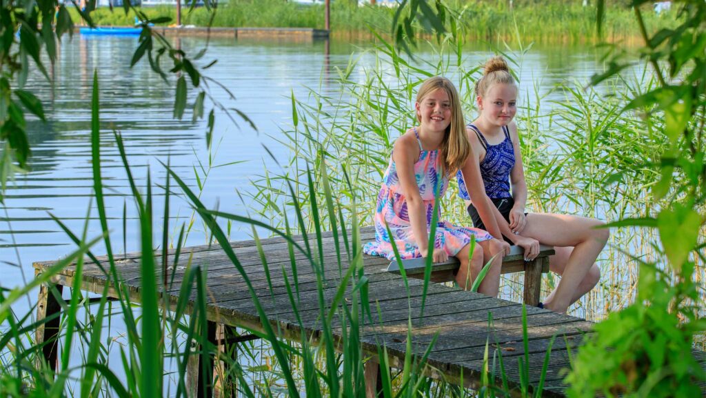 Twee meisjes zitten op de steiger van de waterplas van Molecaten Park De Agnietenberg in Zwolle in Overijssel